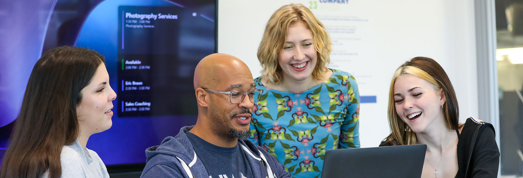 Landing page banner showing several team members happily looking over a computer screen together