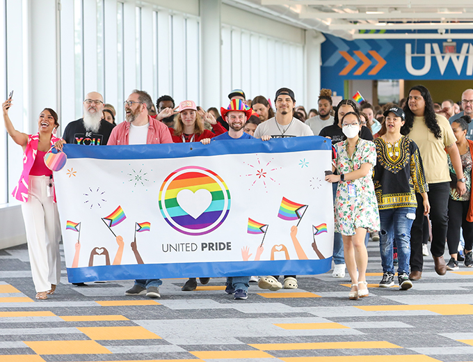 A crowd of happy professionals carrying a UWM United Pride banner for Pride month