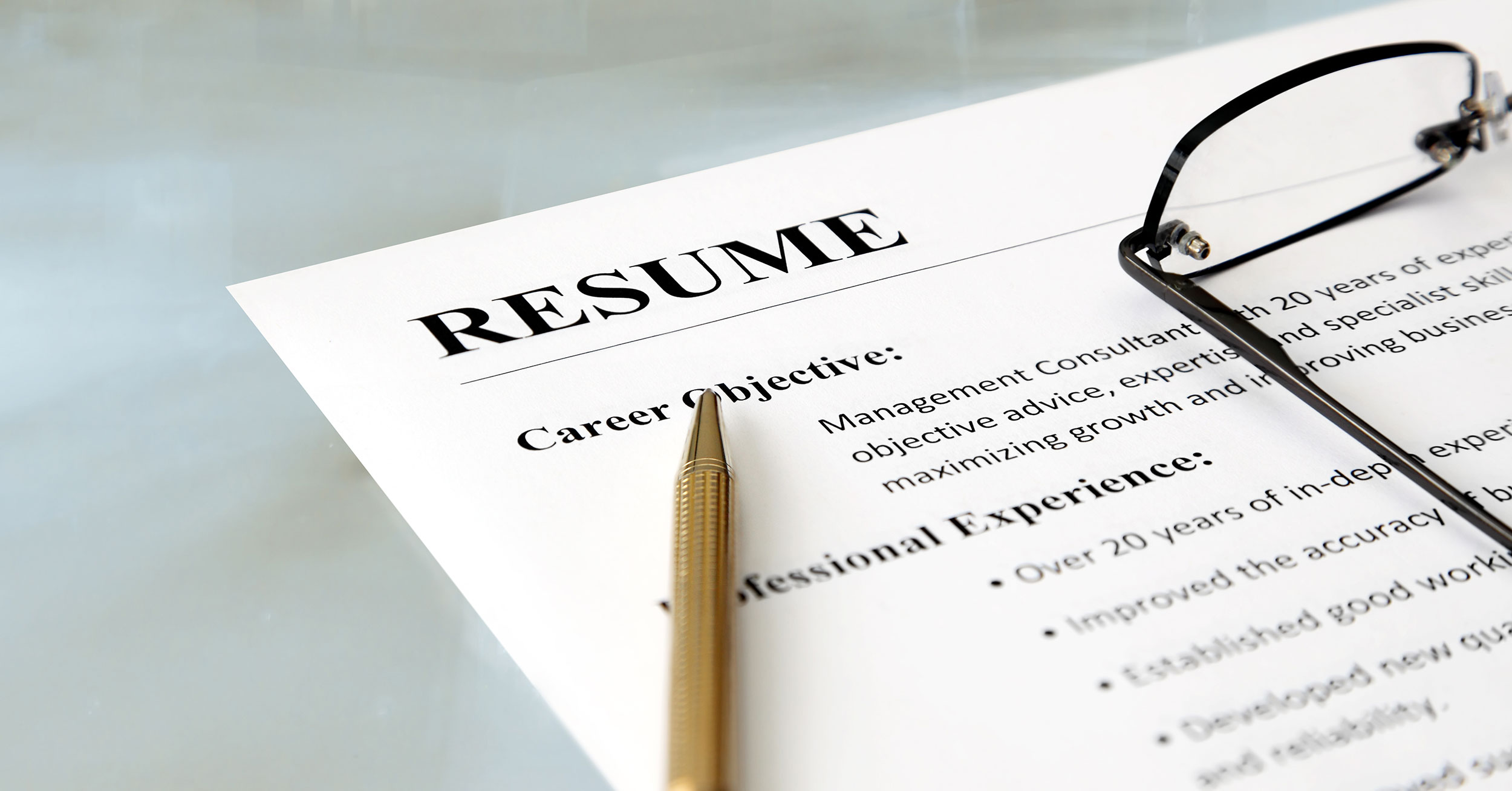 A resume with a pen and glasses on a table. 